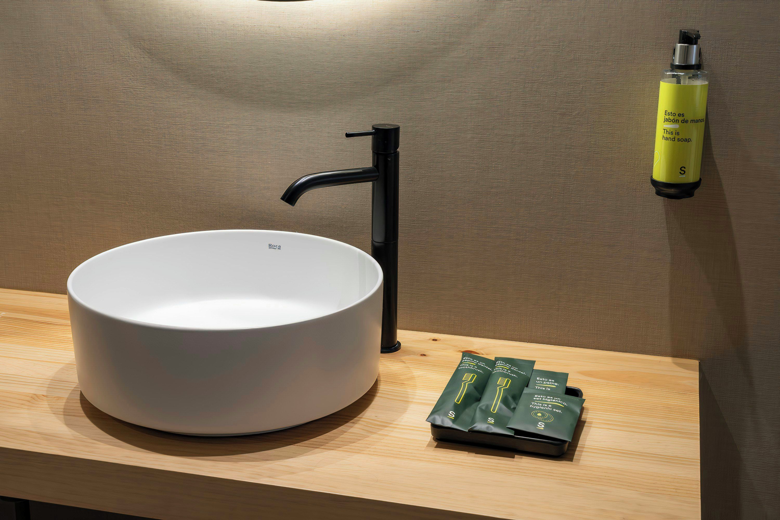 A bathroom with a white sink, a black faucet, and a yellow hand soap dispenser on the wall.