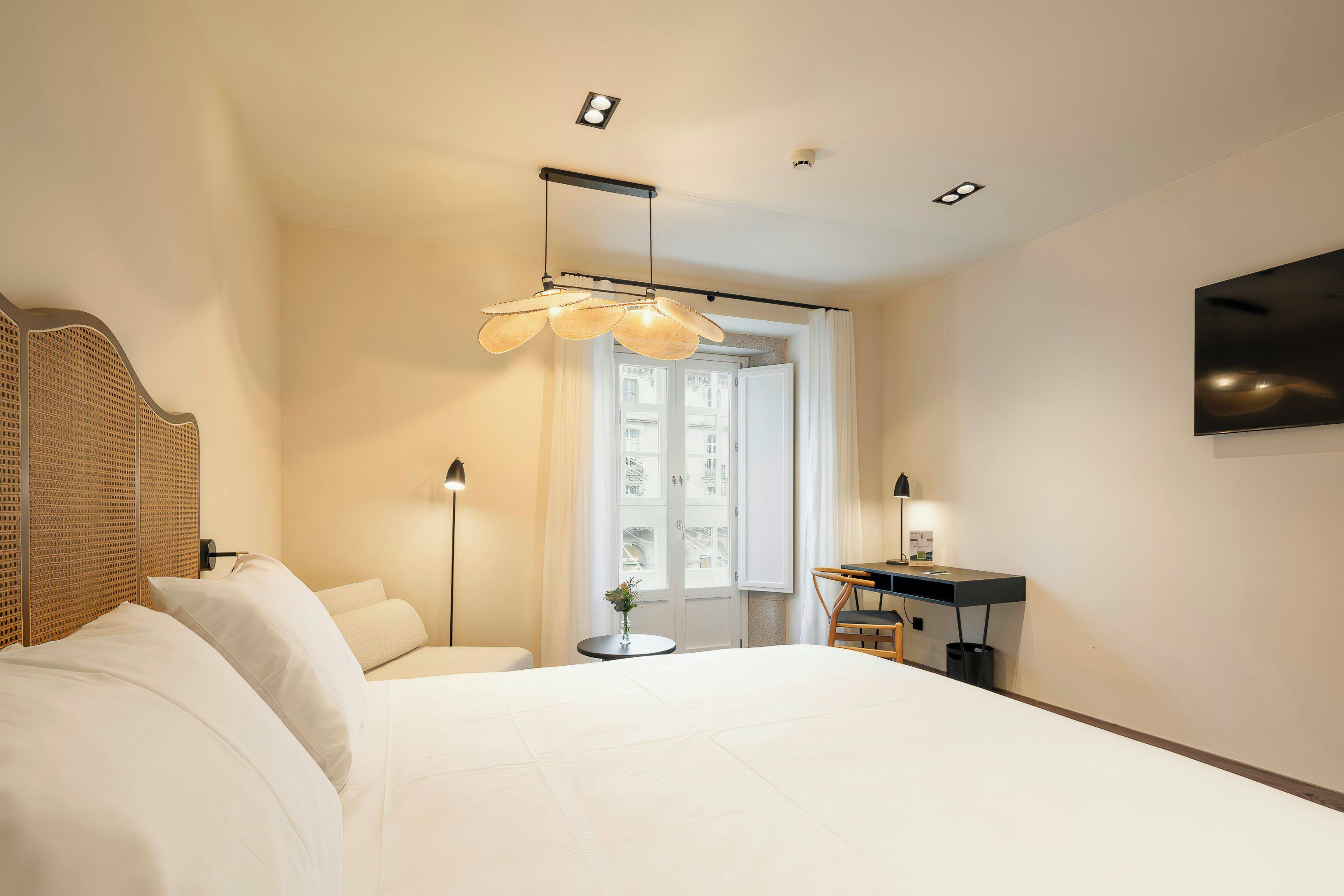 A hotel room with a bed, bedside table, lamp, and a view of the city through a window.
