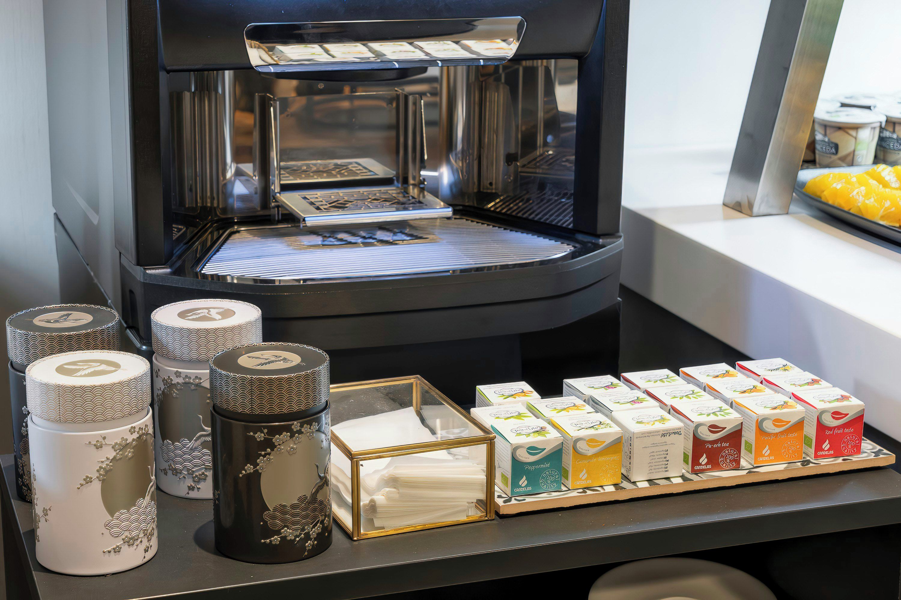 Een koffieapparaat met een dienblad, theezakjes en decoratieve potten op een aanrecht.
