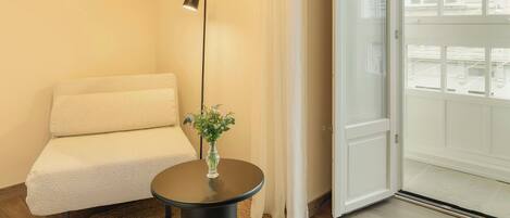 A modern room with a round table, a sofa, a floor lamp, and a large window with a view of buildings.