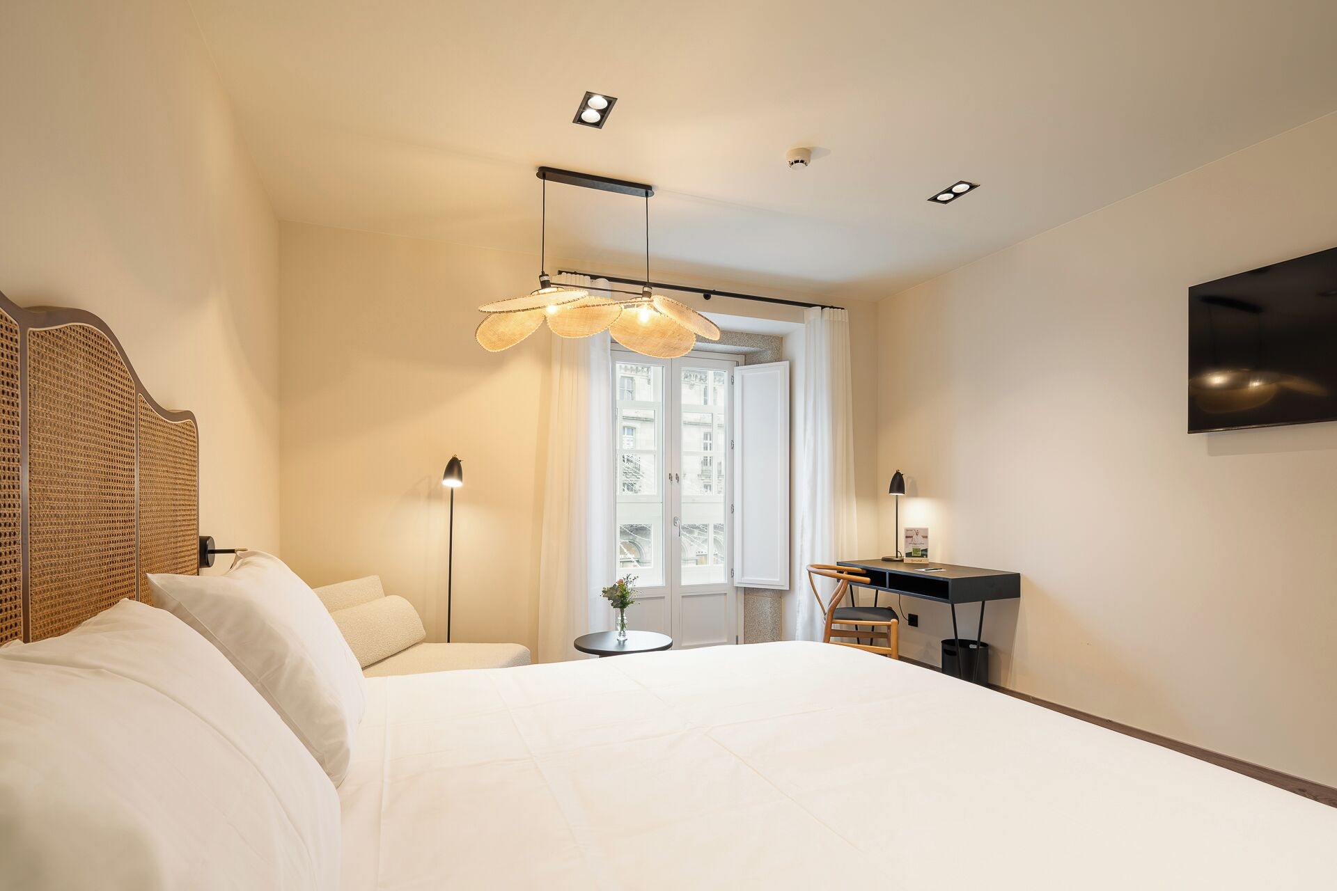 A hotel room with a bed, bedside table, lamp, and a view through a door.