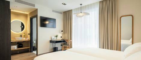 A hotel room with a bed, a desk with a chair, a TV, a mirror, and a bathroom with a sink and toilet.