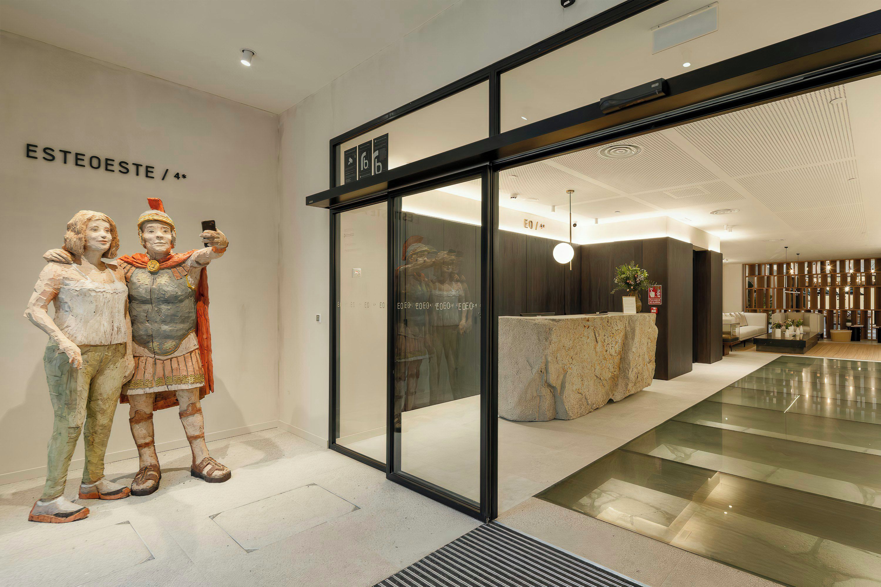 A modern interior with a reception desk, a seating area, and a glass wall displaying a sculpture.