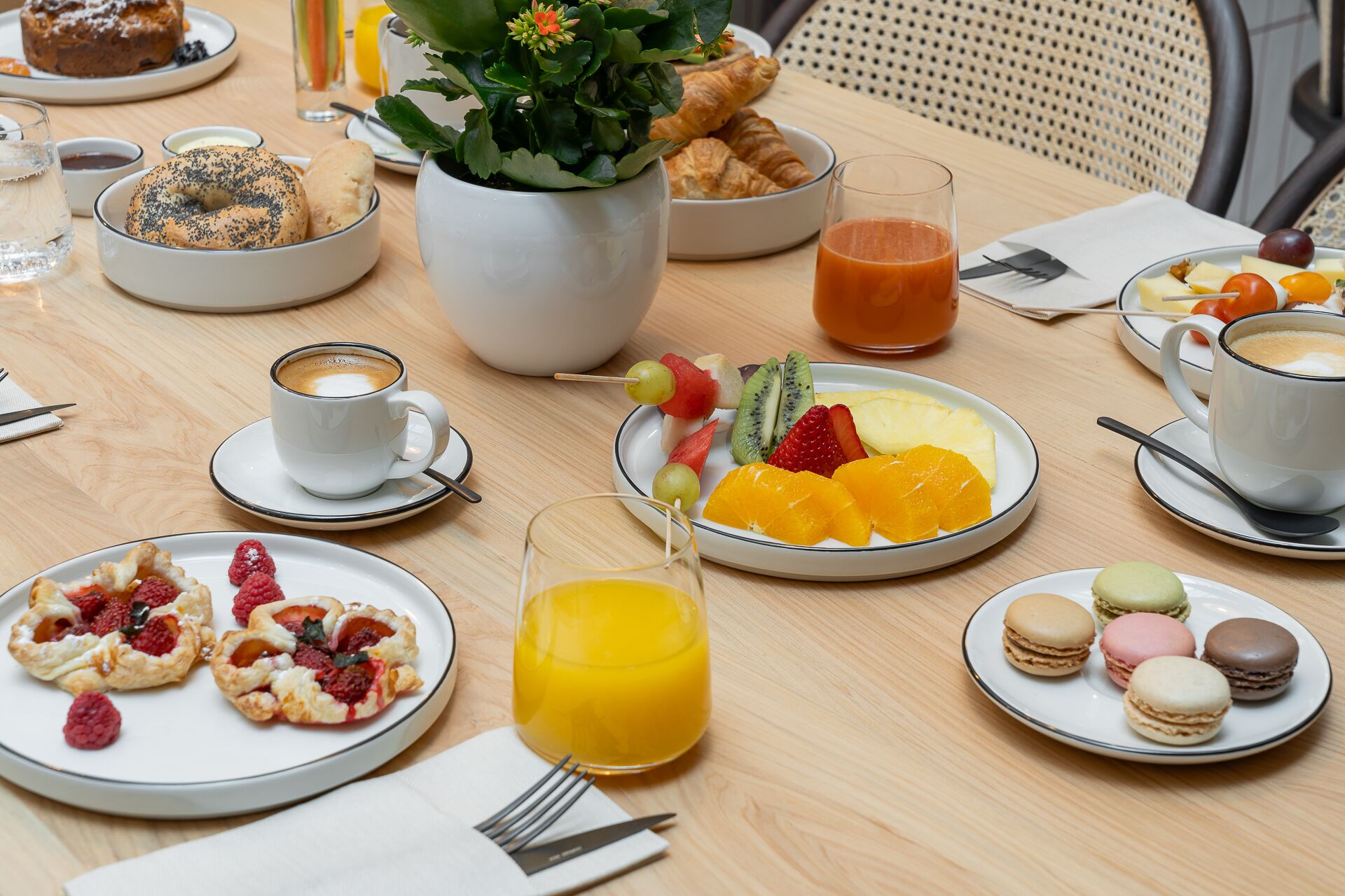 Een ontbijttafel met croissants, gebak, fruit, sap, koffie en macarons.