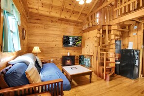 Ein Holzblockhaus-Innenraum mit Bett, Tisch, Kamin, Fernseher und Kühlschrank.