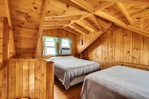 Una cabaña de madera con dos camas, una ventana con cortinas y techo inclinado.