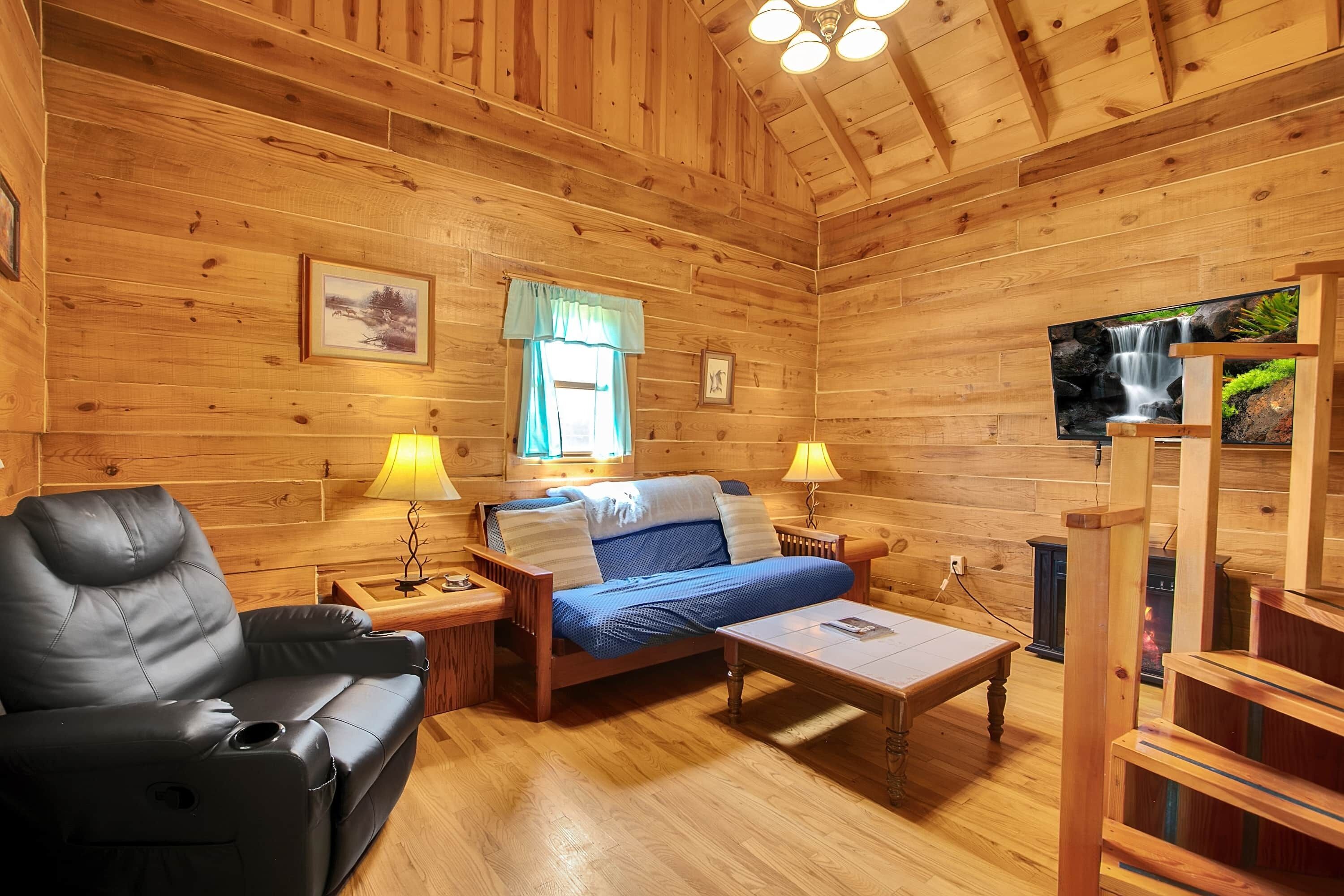 Ein Holzblockhaus im Inneren mit einer Couch, einem Bett, einem Tisch und einem Fernseher.