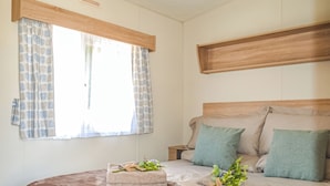 Une chambre à coucher avec un grand lit, deux oreillers, une table de chevet et une fenêtre avec des rideaux.