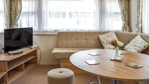 Un salon confortable avec un canapé, une table ronde, un téléviseur posé sur un meuble en bois et une fenêtre avec des rideaux.