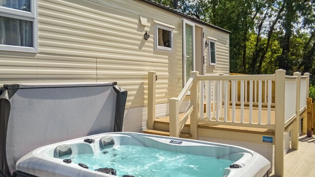 Un bain à remous situé à côté d’une maison mobile, avec une terrasse en bois et une clôture blanche.