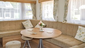 Un salon chaleureux avec une table ronde en bois, un canapé beige et des rideaux à motifs floraux.