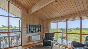 A spacious room with large windows, a flat-screen TV, a dining area, and a seating area with a coffee table.