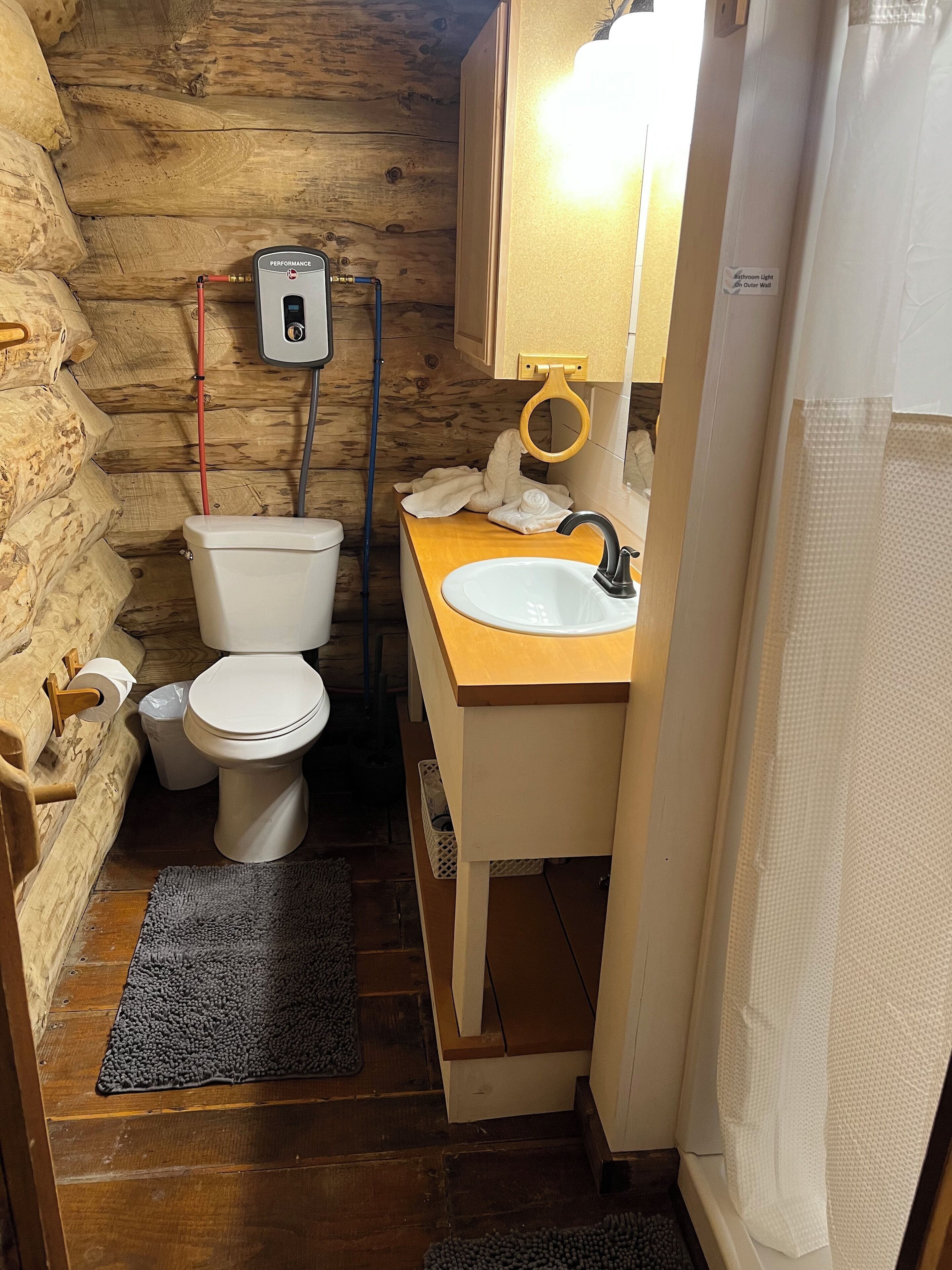 Une petite salle de bain au décor intérieur en bois, avec des toilettes blanches, un lavabo et un rideau de douche.