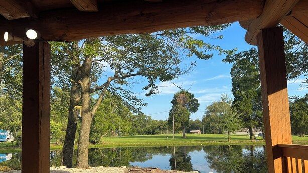 A wooden gazebo with a gravel path leading to a pond, surrounded by trees and a grassy area.