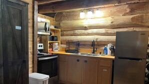 A compact kitchen with wooden walls, a stainless steel refrigerator, a microwave, a coffee maker, and a sink.