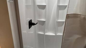 Baño con box de ducha blanco, desagüe visible y toallero.