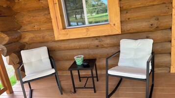 Une cabane en rondins avec deux fauteuils blancs rembourrés et une petite table sur laquelle se trouve une tasse verte.