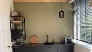 Una cocina compacta con techo de madera, encimera negra y ventana con persianas.