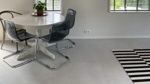 Un comedor moderno con una mesa redonda, cuatro sillas, un cuadro enmarcado y ventanas amplias.