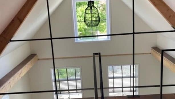 Habitación en el ático con techo inclinado, vigas de madera y ventana con vista a la vegetación.