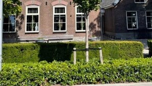 Un edificio de ladrillo de dos pisos con techo a dos aguas, ventanas amplias y un seto bien cuidado al frente.