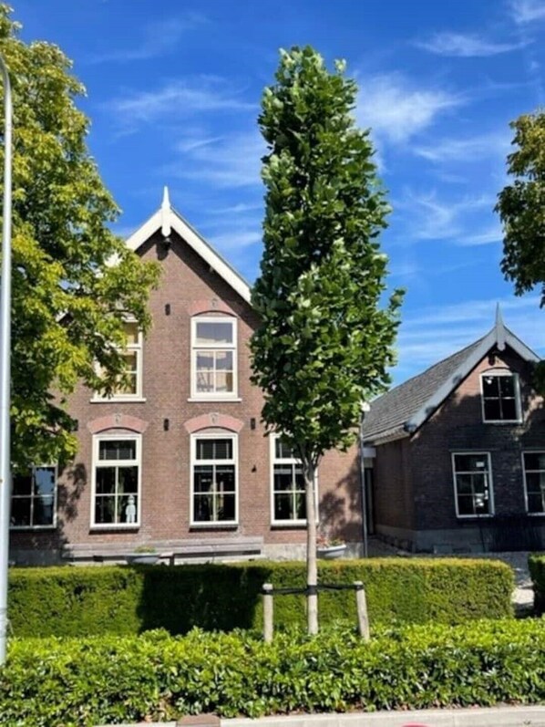 Un bâtiment en briques de deux étages, doté d’un toit à pignon, de grandes fenêtres et d’une haie bien entretenue à l’avant.