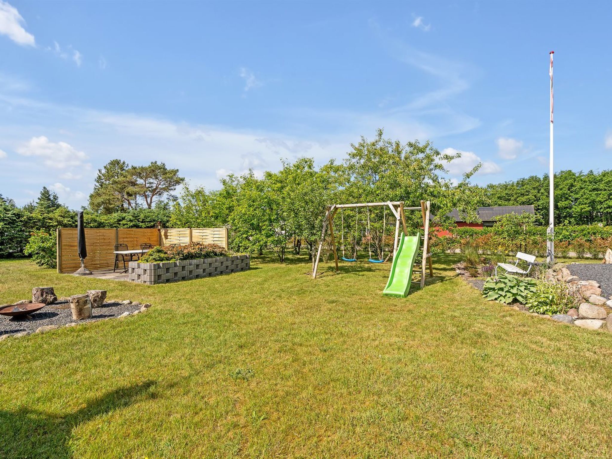 A backyard with a swing set, a slide, a wooden fence, a table, and a bench.