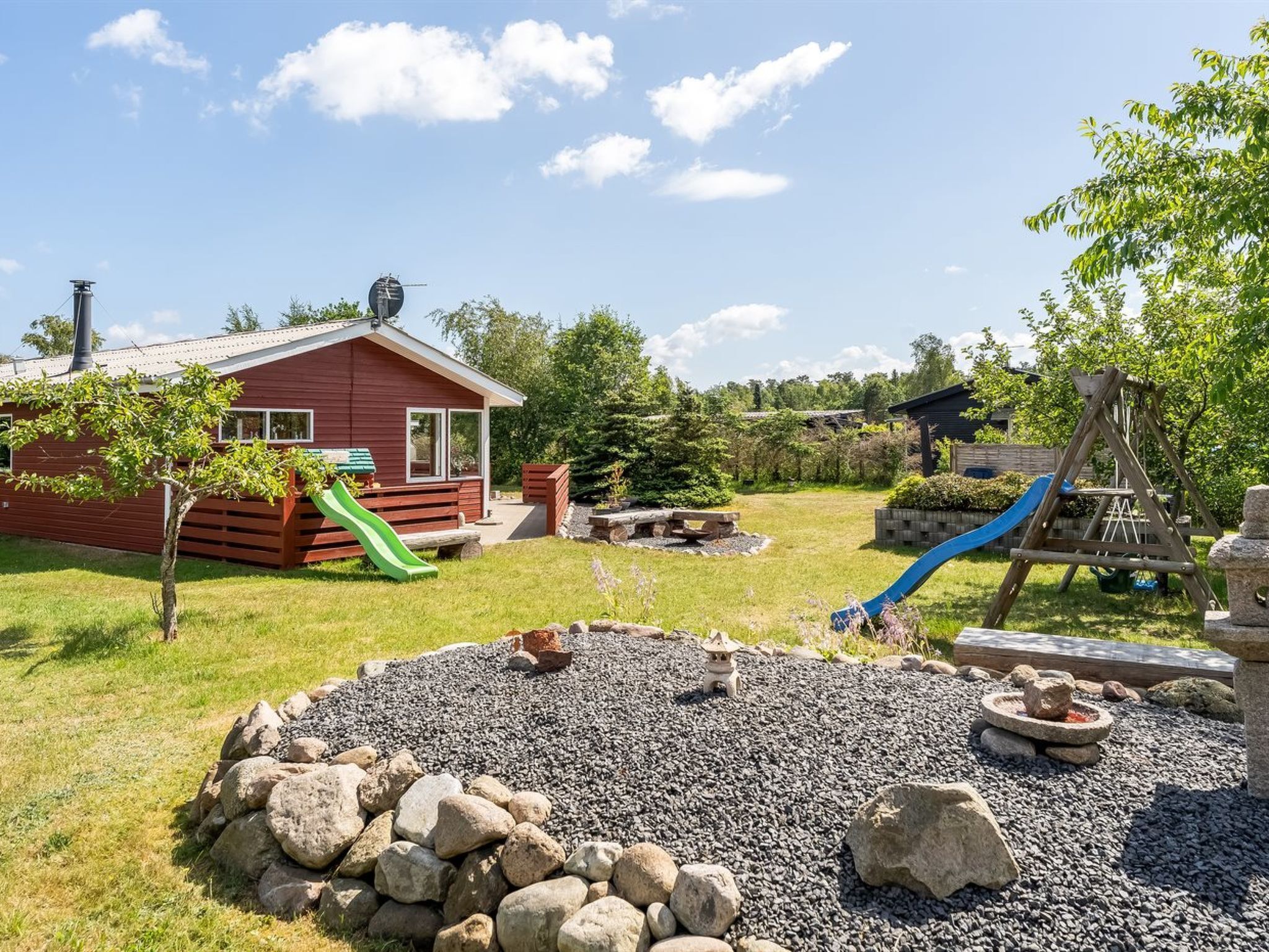 Une cabane rouge avec un toboggan vert, un toboggan bleu et une structure de jeu en bois.
