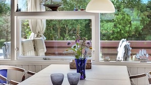 Un coin repas comprenant une table, des chaises, un vase de fleurs et une vue sur l’extérieur grâce à une grande fenêtre.