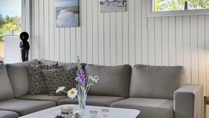 Un salon moderne avec un canapé gris, une table basse blanche ornée de fruits et d’un vase de fleurs, et un tableau accroché au mur.