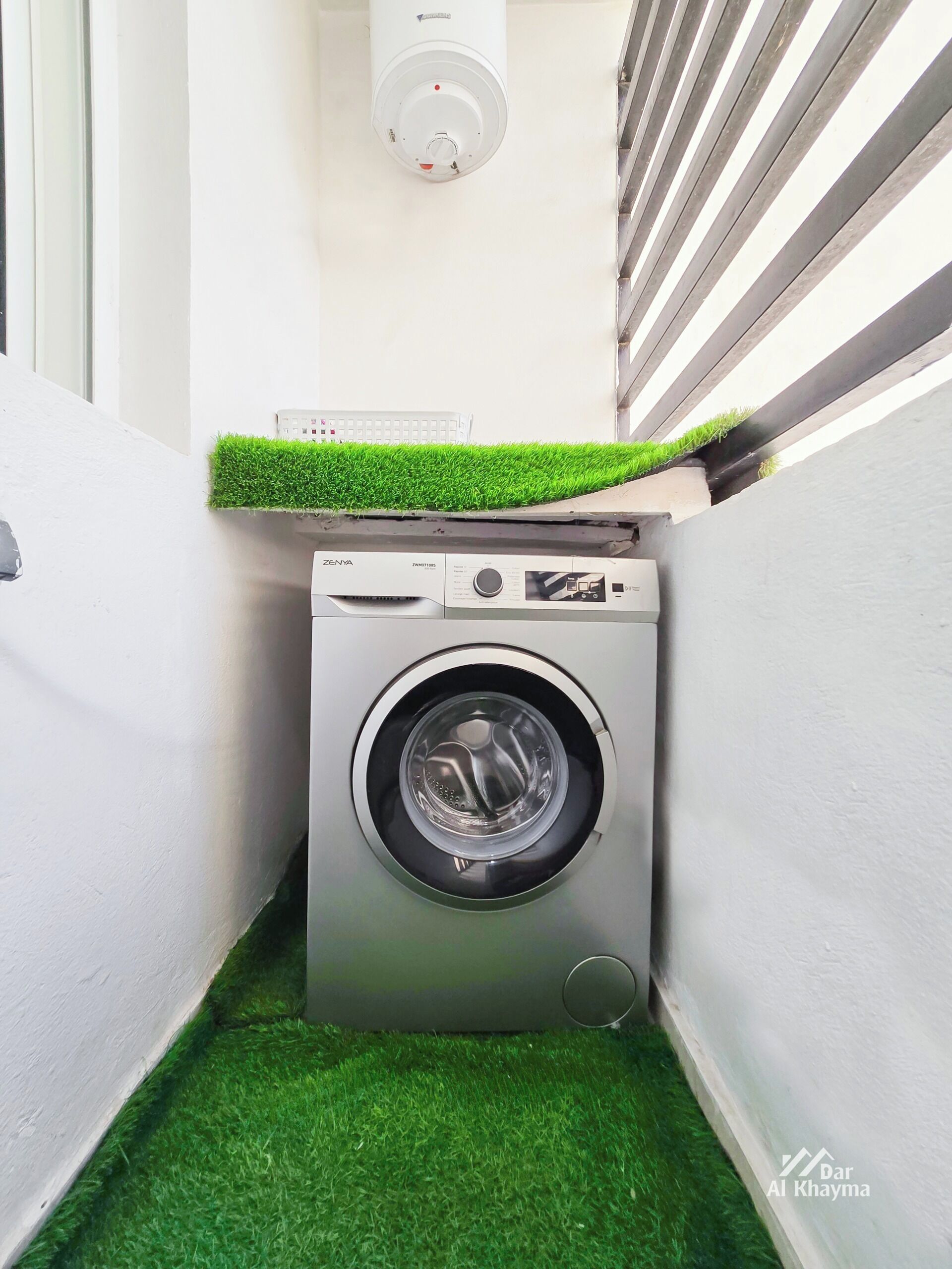 Een kleine wasruimte met een wasmachine, een klein plankje met een toetsenbord en vloerbedekking van kunstgras.