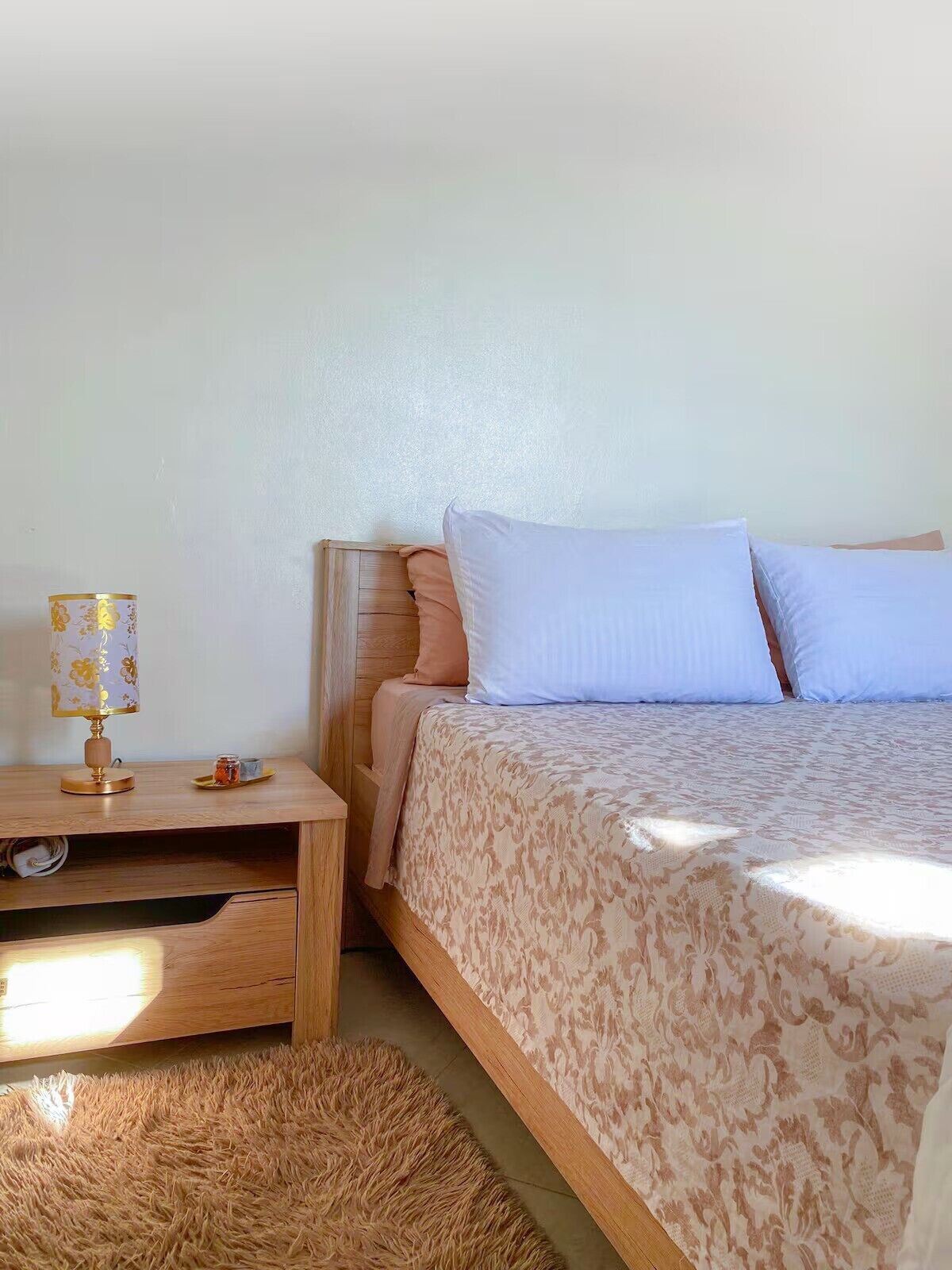 Un dormitorio con una cama de madera, una mesita de noche con una lámpara y un tapete mullido.