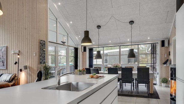 Une cuisine moderne dotée d’un grand îlot central, d’appareils électroménagers en acier inoxydable, de luminaires suspendus et offrant une vue sur l’espace repas extérieur.