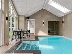 A modern indoor pool area with a clear view of the pool, a seating area with chairs, and a door leading to another room.