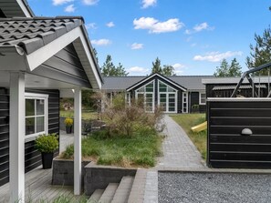 En boligejendom med en overdækket terrasse, en sti der fører til et hus med store vinduer, og en indhegnet have.