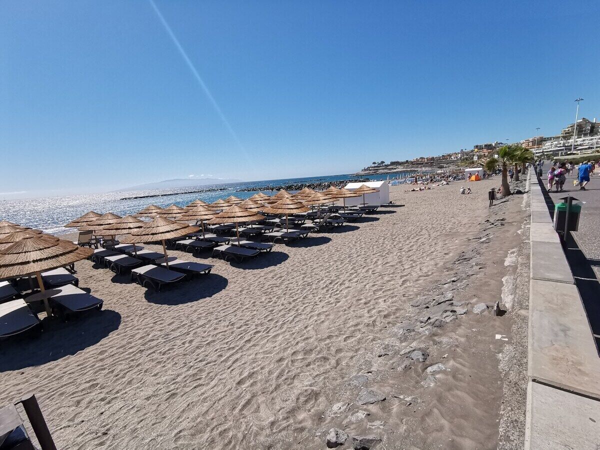 Una platja amb files de gandules i sombrerets de palla, cel clar i una vista llunyana d'edificis.
