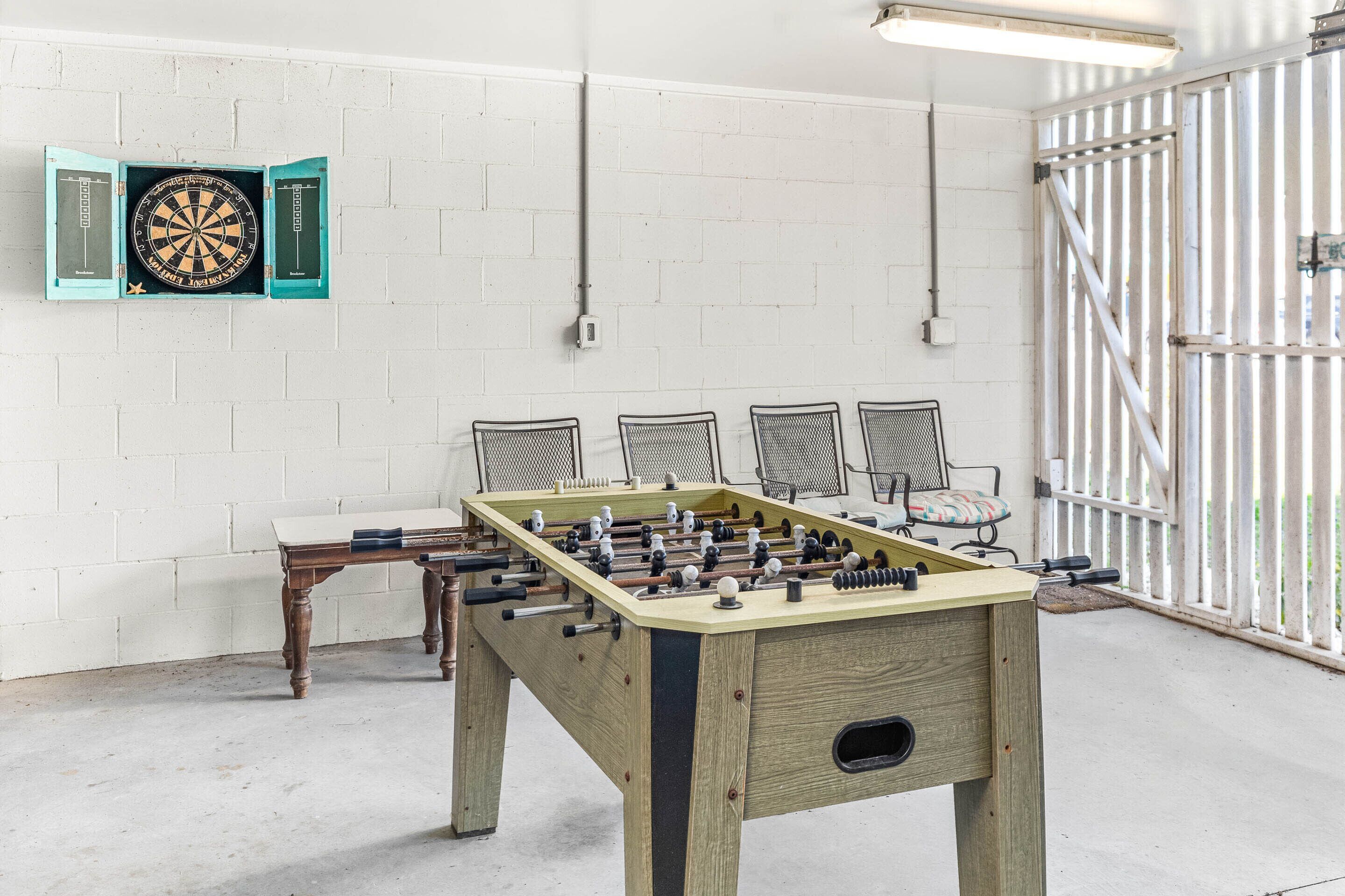 A foosball table in a room with a dartboard and chairs.