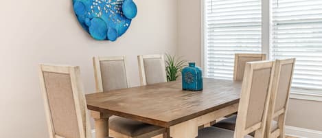 A dining area with a wooden table, six upholstered chairs, and a blue decorative wall piece.