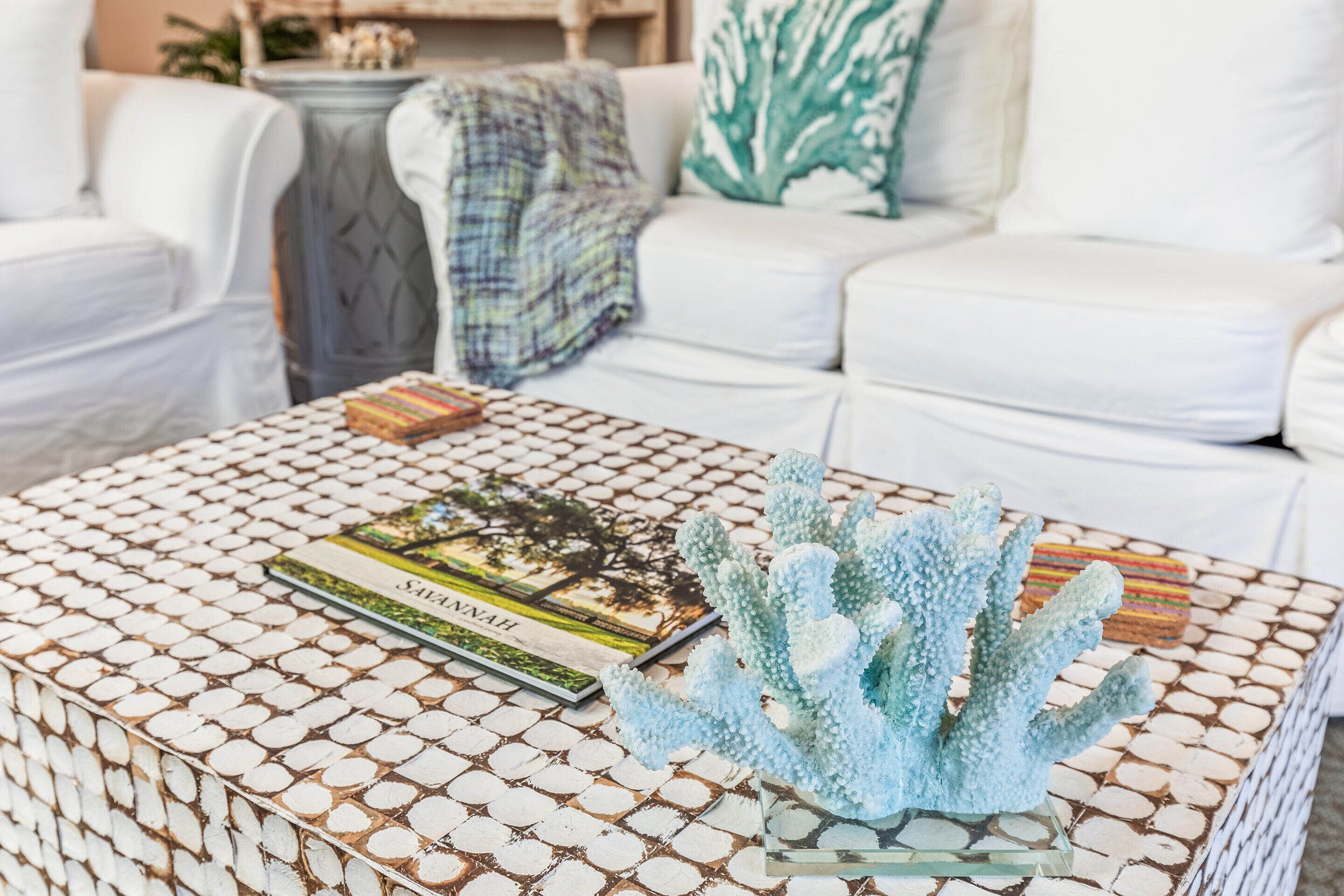 Un sofá blanco, una mesa de centro con estampado que sostiene un libro y una escultura de coral azul.