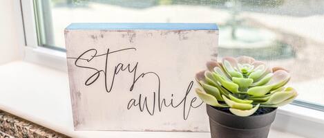A sign with the text "Stay awhile" and a potted succulent plant on a windowsill.