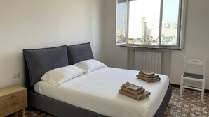 A bedroom with a bed, a window, a radiator, a chair, and a nightstand.