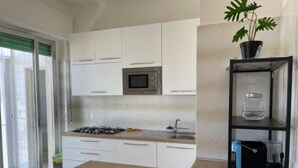 A modern kitchen with white cabinets, a wooden countertop, a gas stove, a microwave, and a black shelving unit with a potted plant.