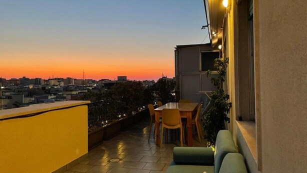 A balcony with a table and chairs, a sofa, and a view of the city skyline at sunset.
