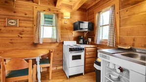 Interior de uma cabana de madeira com fogão, micro-ondas, pia e mesa de jantar com cadeiras.