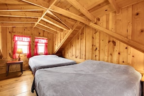 Een houten chalet met twee bedden, een tafeltje en een raam met rode gordijnen.
