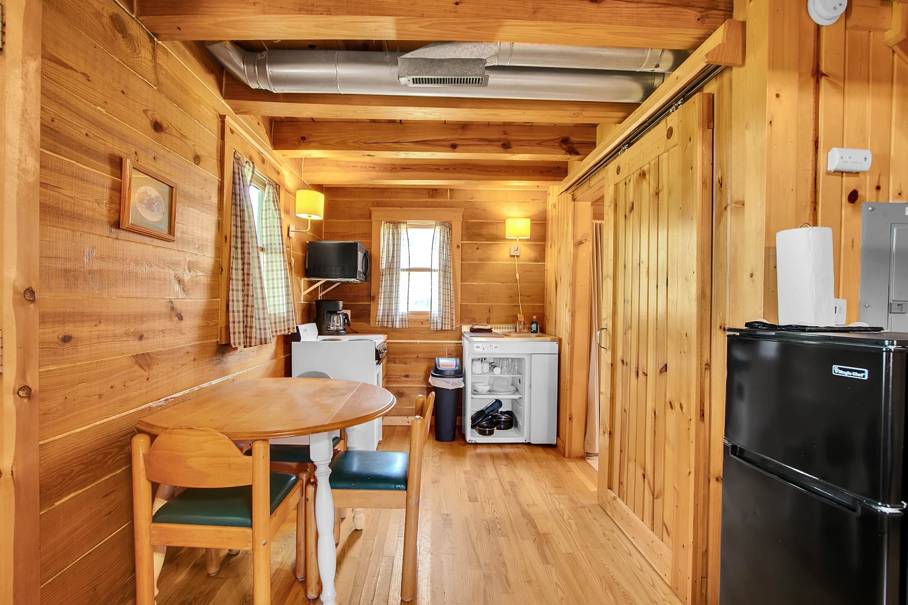 Eine gemütliche Holzblockhütte mit Essbereich, einer Küchenzeile und einem Kühlschrank.