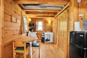 A compact wooden cabin with a dining area, a kitchenette, and a refrigerator.