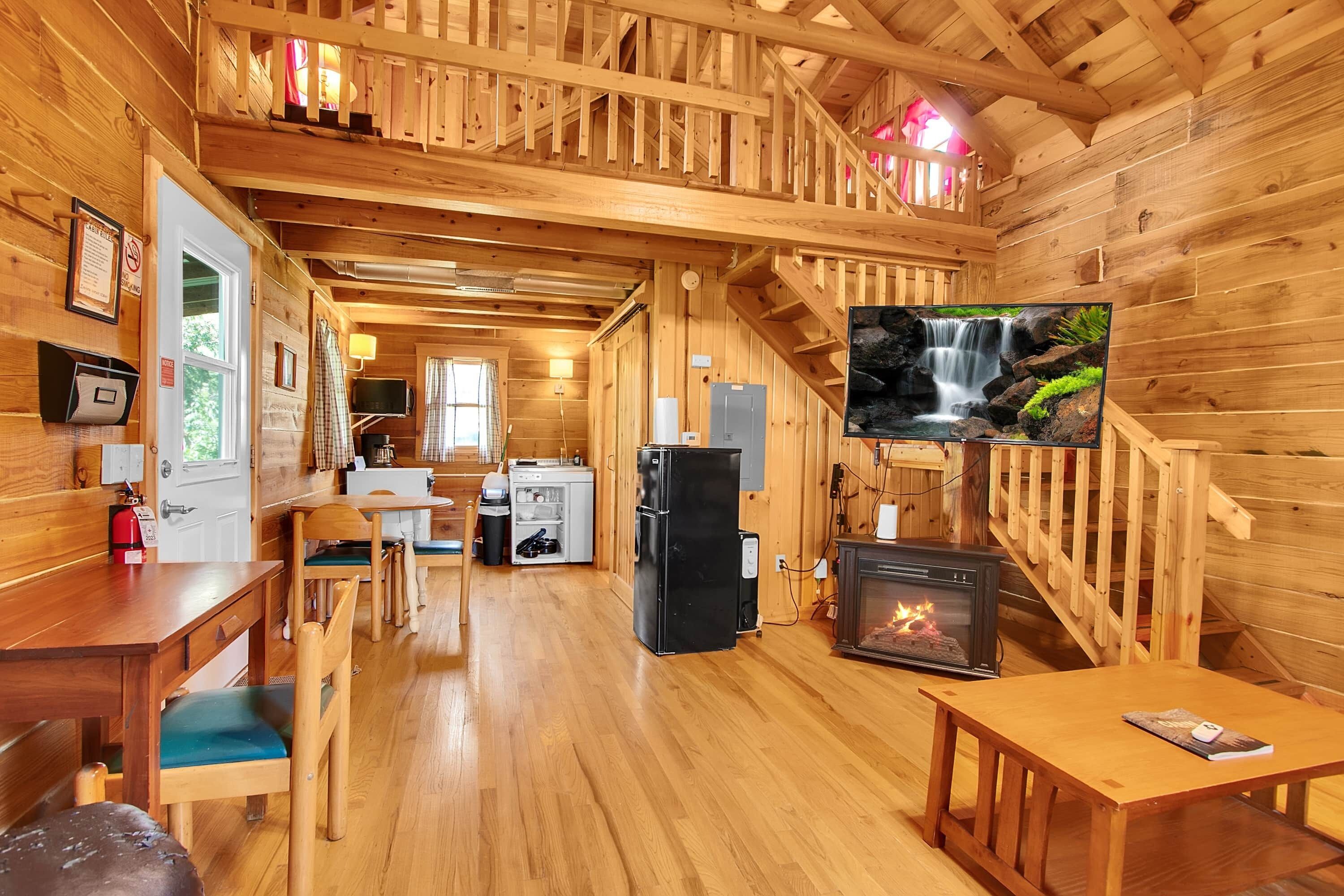 A wooden cabin interior with a dining area, kitchen, and a fireplace.