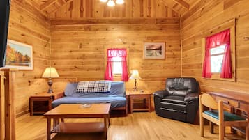 Interior de una cabaña de madera con sofá, sillón, mesa y cama.