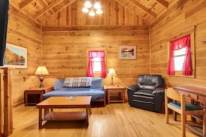 A wooden cabin interior with a sofa, a chair, a table, and a bed.